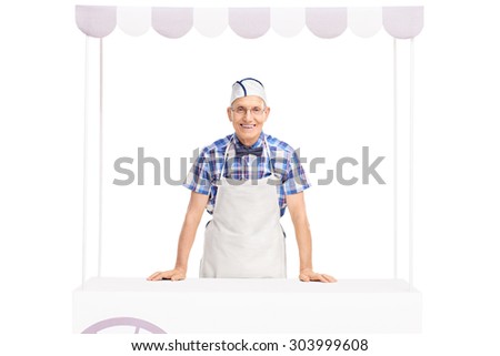 Senior ice cream seller with a white cap and apron standing behind an ice cream stand and looking at the camera isolated on white background