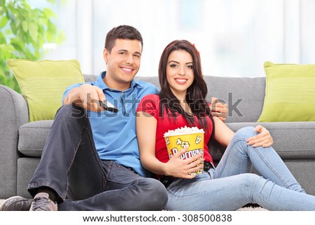 Young couple watching TV seated on the floor at home