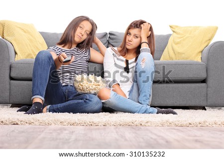 Two bored teenage girls watching TV and changing the channels isolated on white background