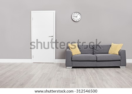 Empty waiting room with a modern gray sofa in front of the door and a clock on the wall