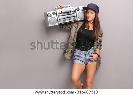 Teenage girl in hip hop clothes holding a ghetto blaster over her shoulder and looking at the camera