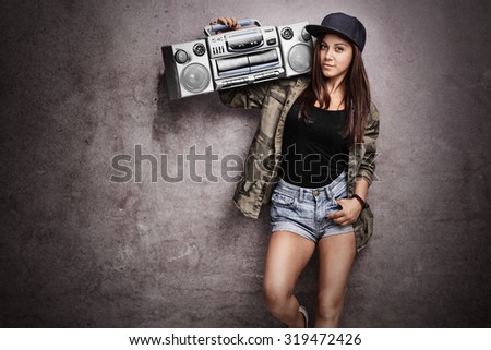 Teenage girl carrying a ghetto blaster over her shoulder and leaning against a rusty gray wall