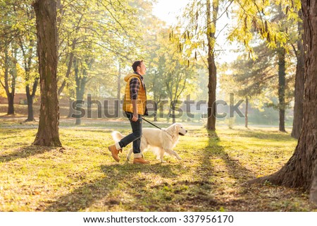 Profile shot of a cheerful young man walking his dog in a park on a sunny autumn day