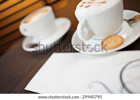 A tilted photo of two cups of cappuccino on a table
