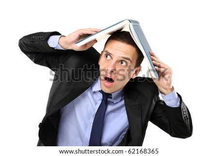 A scared young man in a suit covering his head with an open book isolated on white background