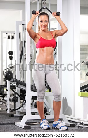 A full length portrait of a woman working out on a fitness equipment at the gym