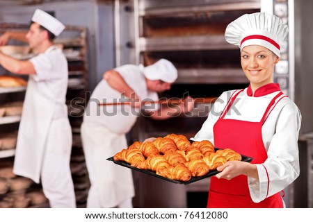 A female baker holding freshly baked croissants in bakery