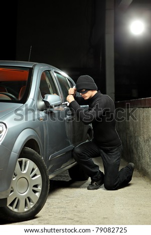 A thief wearing a robbery mask trying to steal a car