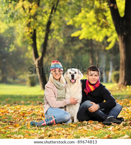 Smiling young man and woman hugging a labrador retreiver dog out in the park