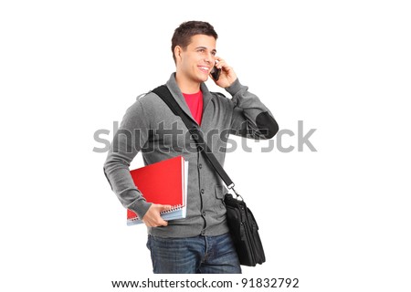 A smiling school boy holding books and talking on a phone isolated on white background
