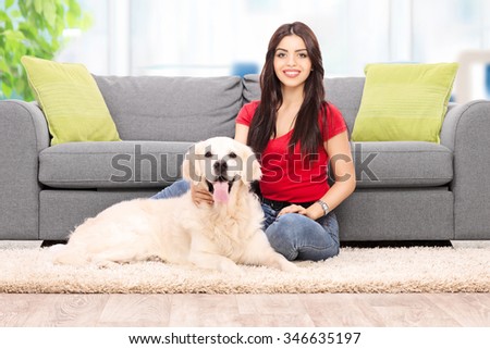 Young girl sitting with her dog at home in front of a gray sofa