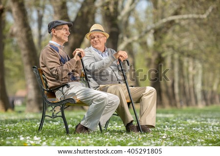 Two old friends sitting on a wooden bench in park and talking to each other