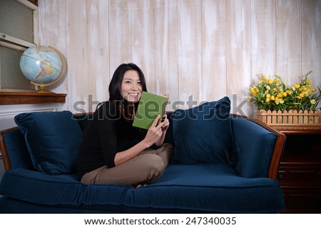 Asian girl sits on a sofa and reads a book
