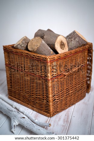 Logs In Wicker Basket , shot on a white wooden floor, close up with white driftwood.