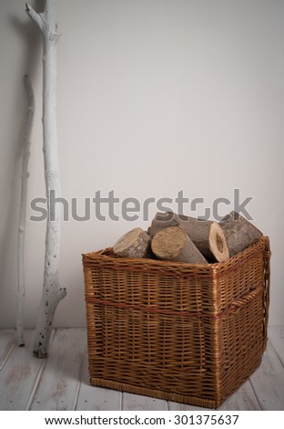Firewood In Wicker Basket against a pale wall with white driftwood, on a wooden floor
