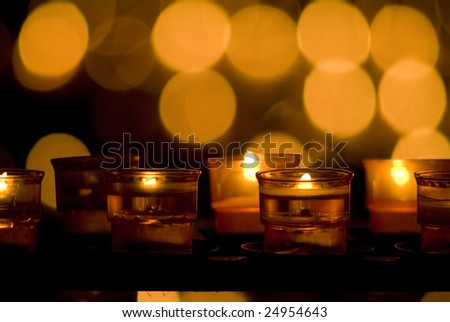 Votive prayer candles in orange glow with blurred flames in background.  Close-up.