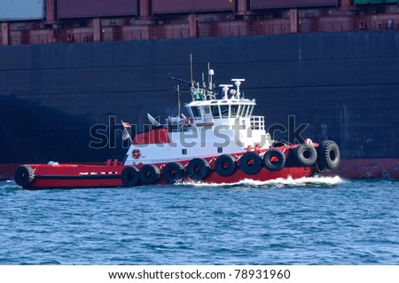 Tug boat moving along side of a cargo ship to get into position to assist in the docking process.