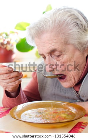 Happy old gray-haired woman eating soup