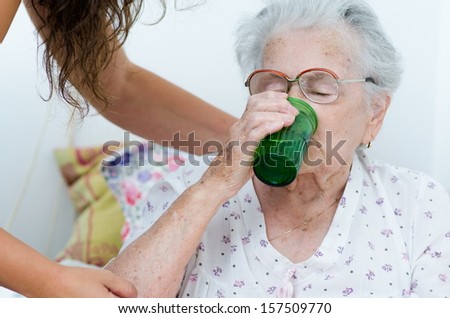 elderly woman drinking water from a glass helpd by her daughter