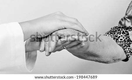 A young hand touches and holds an old wrinkled hand - black and white