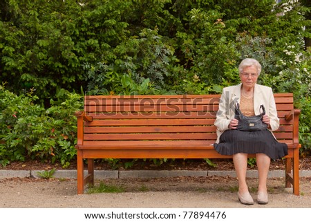 An old lonely woman is sitting on a bench in a park