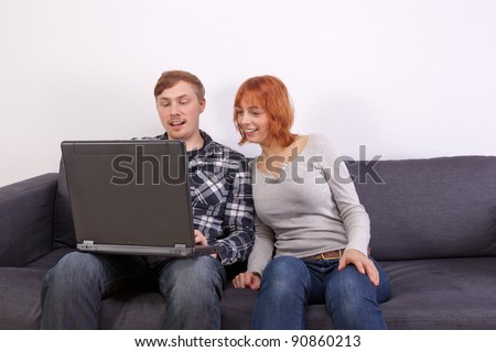 A young couple is sitting on the sofa. The man is showing the woman something on the computer.
