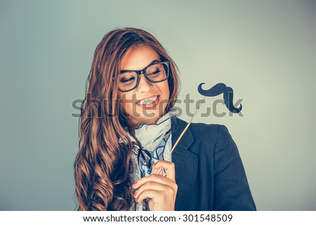 Closeup portrait of attractive playful young happy smiling woman holding looking at mustache on stick isolated on green gray background wall. Positive human emotions facial expressions life perception