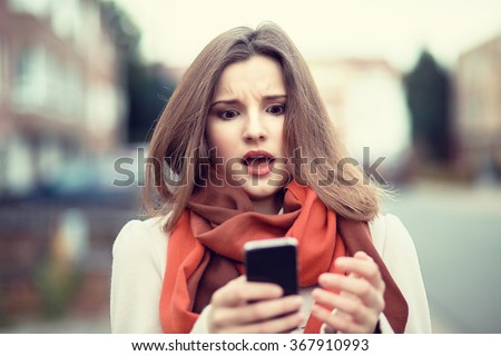 SMS. Closeup portrait funny shocked anxious scared young girl looking at phone seeing bad news photos message with disgusting emotion on face isolated cityscape background. Human reaction, expression