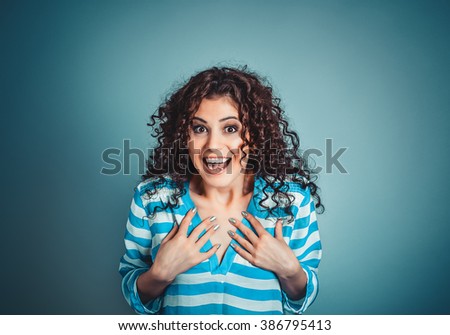 Wow. Closeup portrait young woman beautiful girl with long brown curly hair looking excited holding her mouth opened hands on chest isolated blue wall. Shocked amazed surprised Positive human emotion