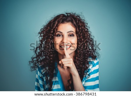 Woman wide eyed asking for silence secrecy with finger on lips hush hand gesture blue isolated background wall. Pretty girl placing fingers on lips shhh sign symbol. Negative emotion facial expression