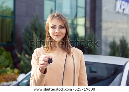 Closeup portrait happy, smiling, young attractive woman, buyer near her new car showing keys isolated outside dealer, dealership lot office. Personal transportation, auto purchase concept