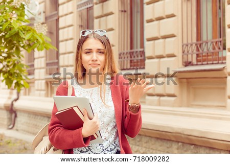 Confused student. Closeup portrait puzzled clueless young woman arm out asking what is problem who cares so what I don’t know isolated college building on background. Negative emotion face expression