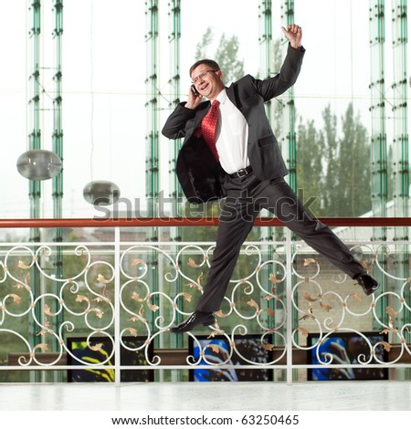 smiling jumping man with mobile phone on background of glass wall
