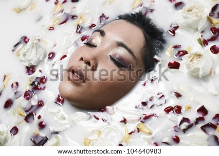 Portrait of beautiful young woman in a milk bath with flowers