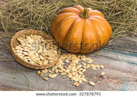Orange pumpkin with seeds on a wooden surface against a background of hay. Wicker dish with pumpkin seeds.