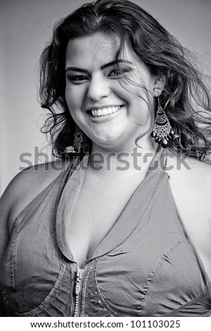 Female Plus size model posing in the studio, chest and face portrait, on grey background. The woman is smiling in a happy manner. Good for concept of health, happiness, dieting, obesity, weight loss.