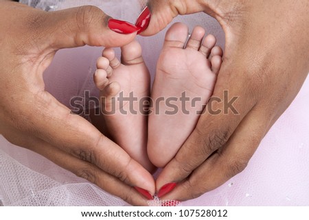 Baby\'s feet in mom\'s palms, forming a heart shape with mother\'s hands. Candid appeal.