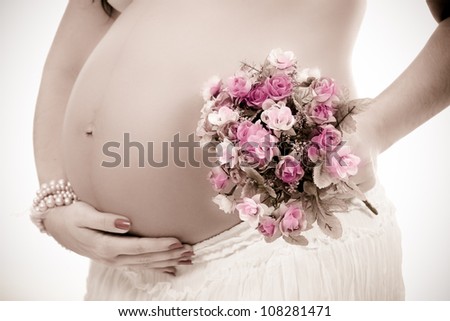 pregnant woman caressing her belly close to pink flowers waiting for the birth. The mother\'s belly is on profile angle. The photo has soft effect to give it the correct feeling.