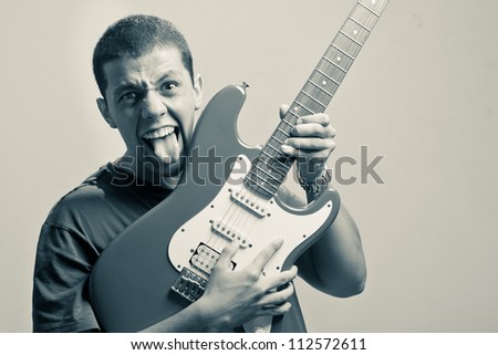 Crazy man playing a solo on his guitar and showing his tongue in furious manner. A dramatic light has been used to give the right appeal to the image. The photo has been edited on a duotone color.