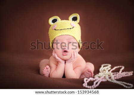 Newborn baby  sleeping, resting on her own hands and elbows, on brown background. Frog hat and frog pose.