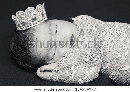 Adorable newborn baby sleeping wrapped on pink lace on brown cushion with a crown on the head.