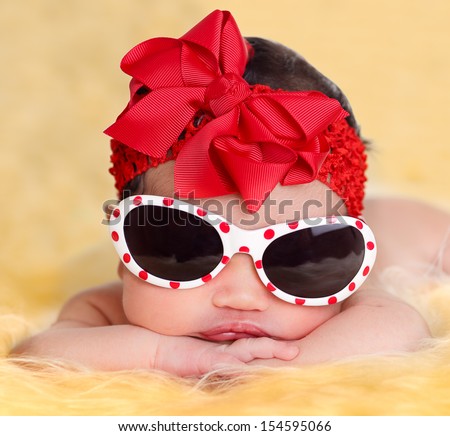 Nice newborn baby girl posing with sunglasses on  yellow fur and white background wearing a red ribbon.