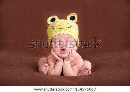 Newborn baby  sleeping, resting on her own hands and elbows, on brown background. Frog hat and frog pose.