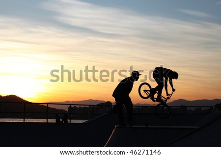 BMX Bike flying off the track with the sea, horizon and sunset in the background. Also shows the perfect silhouette of another guy looking amazed to the BMX.