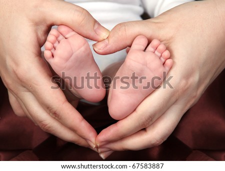 Mother\'s hands forming a heart among her baby\'s feet with a brown cloth on the background.