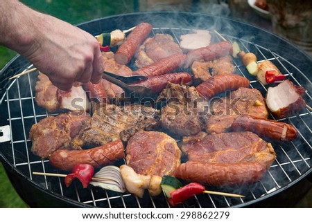 A man uses tongs to turn sizzling sausages grilling on a barbecue packed with meat