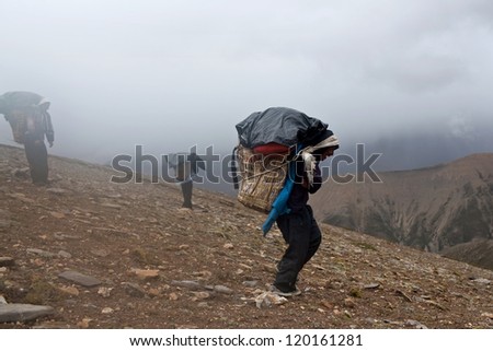 UPPER DOLPO, NEPAL - SEPTEMBER 12: Porters carry heavy load in the Himalaya in time of the Russian ethnographic Expedition on September 12, 2011 in Upper Dolpo restricted area, Nepal
