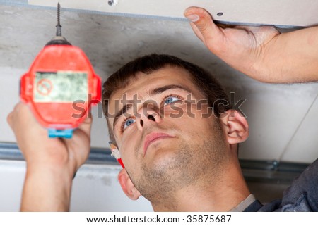Man tie plasterboard screwdriver to guide rails and looks closely at the ceiling. Sharpness to face