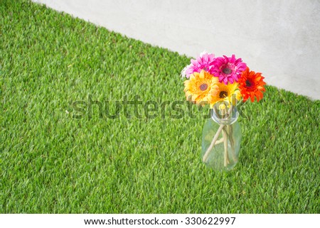 artificial flowers in vase on artificial grass with concrete wall