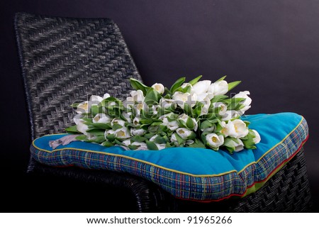 White bouquet of tulips on black chair with blue cushion